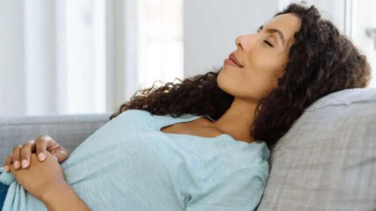 Vrouw ontspant met gesloten ogen in de zetel – relaxatietherapie en ademhalingsoefeningen tegen stress